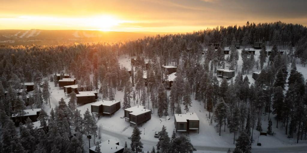 Raised wooden cabins among snow-covered pines on a wooded slope.