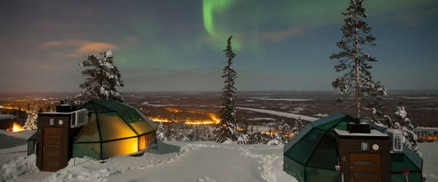 Glass-roofed cabins on snow under a green northern sky.