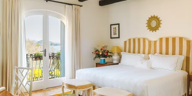 A bedroom with white linens and an arched balcony looking out over water.