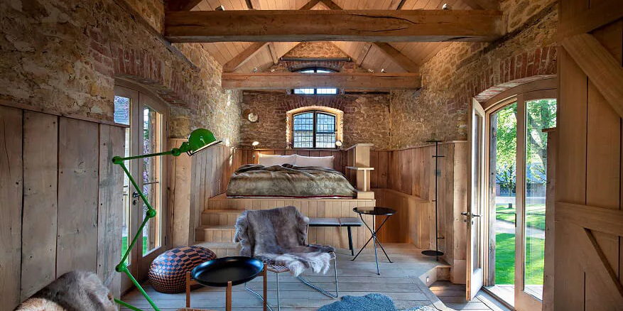 A stone and timber guest room with a bed on a raised wooden platform.