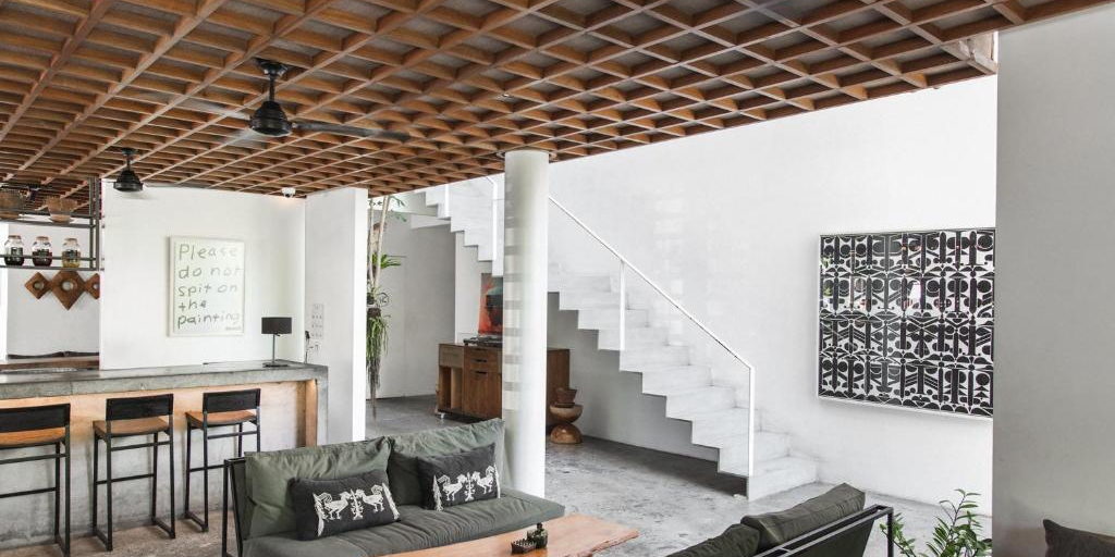 An open lounge with a white stair, a wooden ceiling grid and seating.