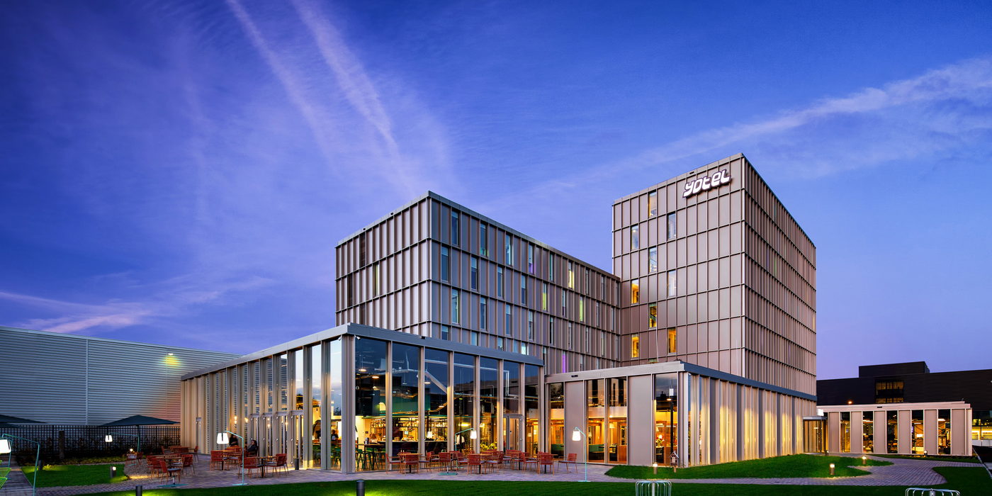 The YOTEL Amsterdam building at dusk, seen across a lawn with a lit ground floor.